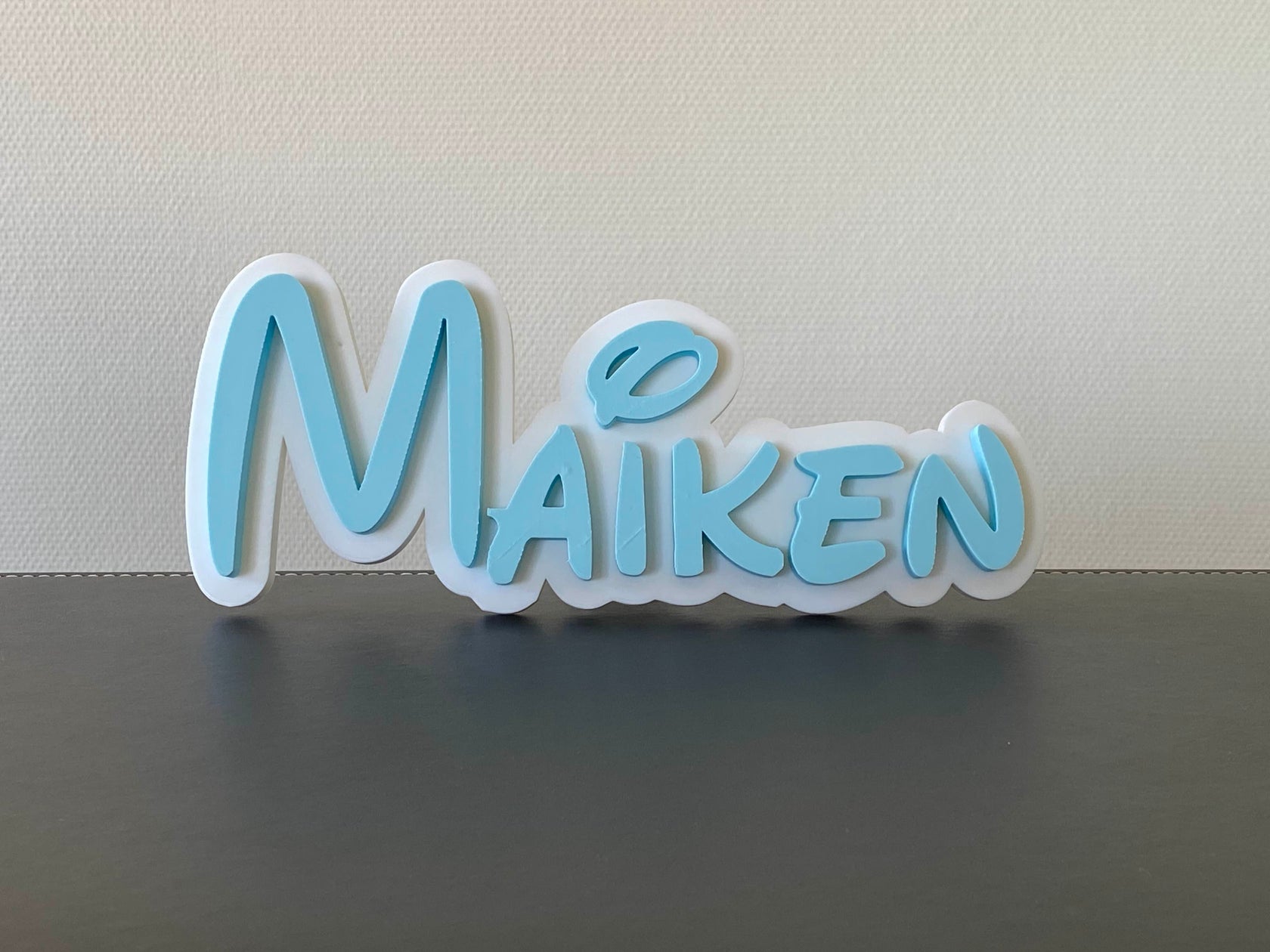 Decorative name sign with 'Maiken' in light blue on a white background